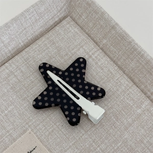 Detail view of a star-shaped black hair clip with grey polka dots on a duckbill clip