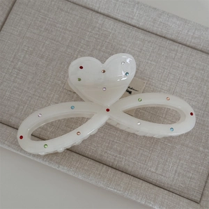 Detailed view of a cream heart hair claw clip with colorful rhinestones on a display box