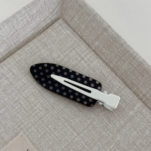Detailed top view of a black hair clip with white polka dots on a beige texture