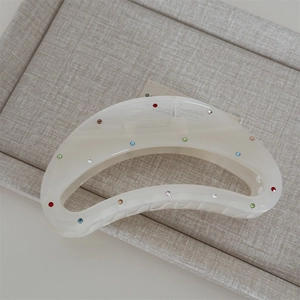 Detail of ivory crescent hair claw clip featuring colorful rhinestones on linen tray