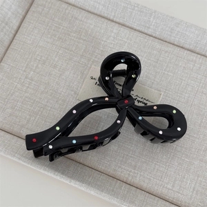 Detailed view of black bow hair claw clip with vibrant colorful rhinestones on grey fabric