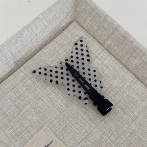 Detailed view of butterfly hair clip with black polka dots on a white acetate surface
