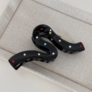 Detailed macro view of black S-shaped hair claw clip with colorful sparkling rhinestones