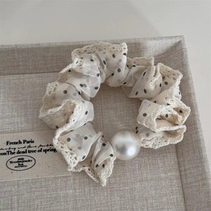 Macro detail of cream mesh hair scrunchie with black dots, lace trim and pearl accent