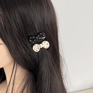 Detailed close-up of glossy black and white polka dot bow hair clip on dark hair