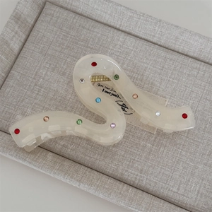 Elegant wavy hair claw clip in creamy resin with colorful rhinestones on grey tray