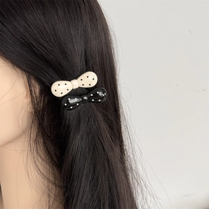 Detail view of black and white polka dot bow hair clips worn on long dark hair side