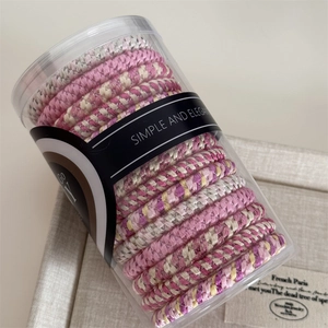 Detail of woven spiral hair ties in pink and beige inside a transparent cylinder jar