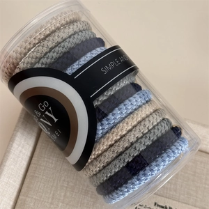 Detail of woven elastic hair ties in cool tones stored in a clear cylindrical bottle
