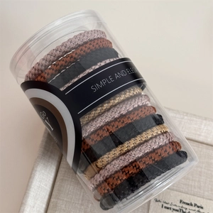 Detail view of woven high-elastic hair ties in neutral earth tones in clear cylinder box