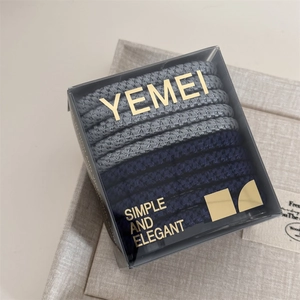 Detail of high-elasticity hair ties in dark grey and navy blue within a premium clear gift box