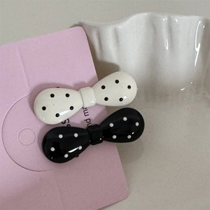 Detailed view of black and white polka dot bow hair clips on pink card packaging