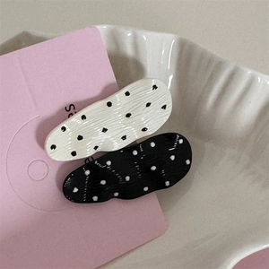 Detail showing two wavy polka dot hair clips in black and white on a ceramic plate