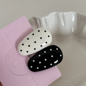 Close-up of black and white polka dot hair clips with glossy finish on pink card