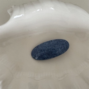 Detail view of oval denim twill hair clip on a cream decorative ceramic shell tray