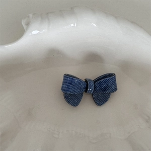 Detail view of denim texture acetate bow hair clip resting on a textured cream tray