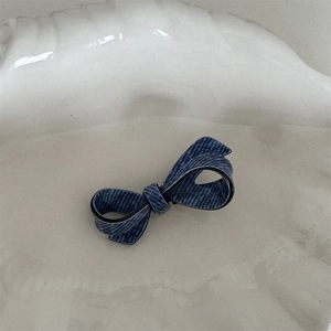 Detail of blue denim fabric bow hair clip featuring black trim and textured woven patterns