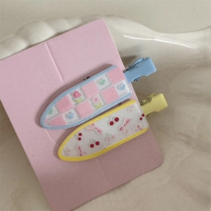Close-up of two floral hair clips with heart and cherry patterns on pink card