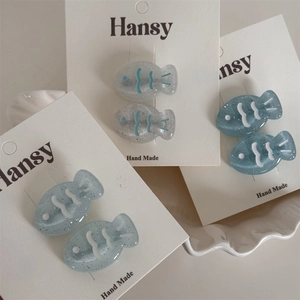 Detail of glittery resin fish-shaped hair clips in light blue and greyish blue colors