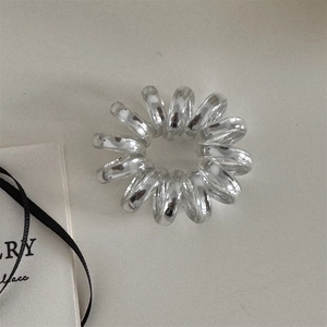 Détail d'un élastique spirale argenté au fini métallique sur fond texturé minimaliste