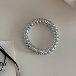 Détail d'un élastique spirale argenté au fini métallique brillant sur fond beige doux