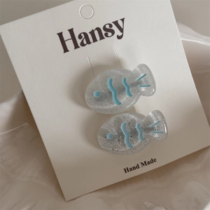 Detail of two fish-shaped hair clips in taupe resin with silver glitter and blue patterns