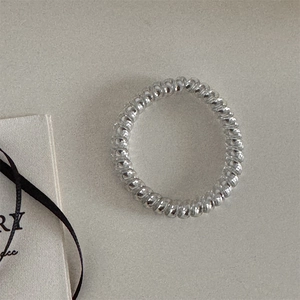 Gros plan détaillé d'un élastique à cheveux spirale argenté sur fond gris texturé