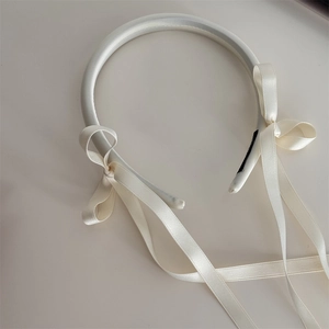 Detailed close-up of cream-white satin bow headband with elegant long trailing ribbons