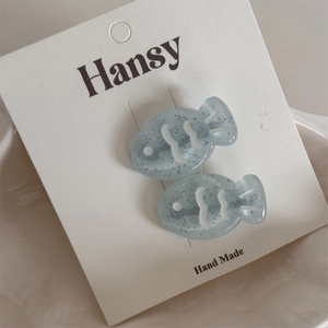 Close-up of two light blue glitter acrylic fish hair clips on a white display card