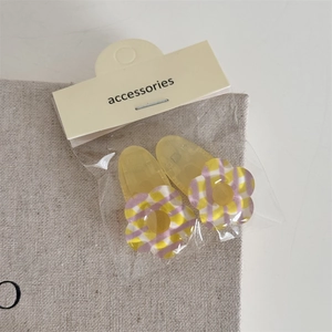 Détail de deux barrettes à fleurs à carreaux jaunes et violets avec emballage