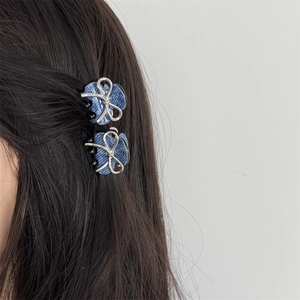 Close-up of small blue denim bow hair claws with silver edges on dark brown hair