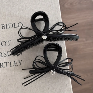 Set de pinces à cheveux noires brillantes avec nœud et breloque cœur argenté sur tissu gris