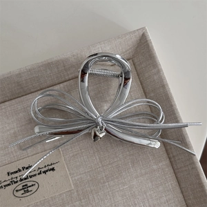 Détail de la pince à cheveux noeud argenté avec pendentif coeur sur support beige