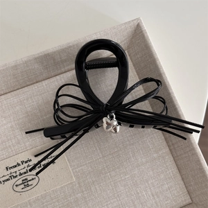 Détail d'une pince à cheveux noire brillante en forme de nœud avec pendentif cœur argenté