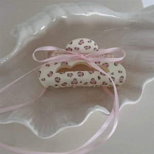 Dettaglio della molletta color crema con stampa leopardata rosa e fiocco in nastro lungo