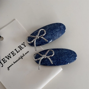 Detail view of oval hair clips featuring blue denim texture and silver bow design