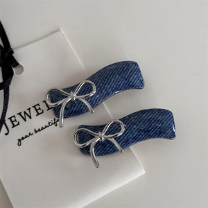 Detail of blue denim textured hair clips with silver metallic bow accents on white card