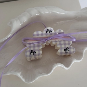 Dettaglio molletta per capelli a quadri viola con fiocco e nastro di raso su vassoio