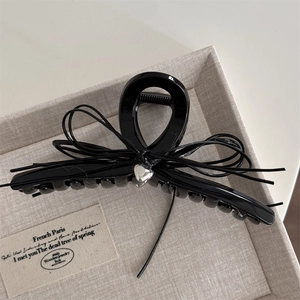 Détail d'une pince à cheveux noire brillante avec un nœud en cordon et pendentif cœur