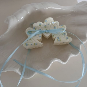 Dettaglio macro della molletta in resina crema con motivi floreali e fiocco in nastro blu