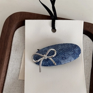 Close-up detail of silver metal bow on blue denim texture acrylic hair clip accessory