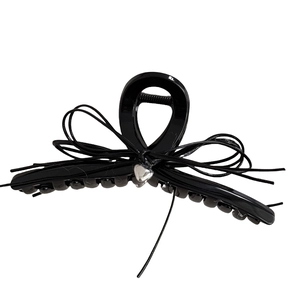 Pince à cheveux noire élégante avec nœud et pendentif cœur argenté sur fond blanc