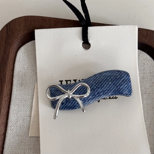 Detailed close-up of blue denim hair claw clip with a shiny silver metallic bow ornament