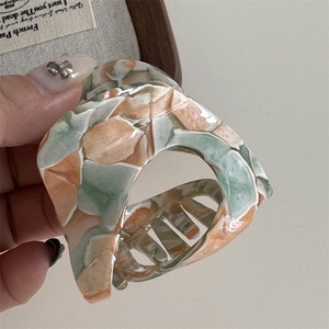 Close-up of marbled acetate shark hair claw clip in green and orange tones