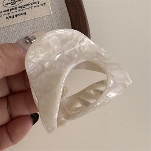 Close-up of cream white acetate hair claw clip with pearlescent finish and metal spring