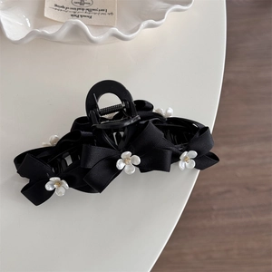 Detailed top view of large black ribbon bow hair claw with white flowers and gold beads