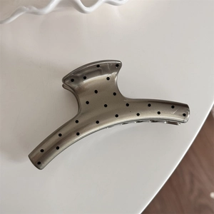 Detail view of champagne gold shark hair clip with elegant black polka dot pattern