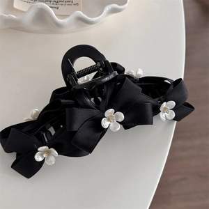 Close-up of black hair claw clip featuring ribbon bows and white floral accents