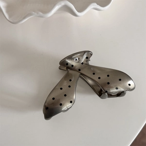Detail view of a silver hair claw clip with black polka dots and subtle glitter finish