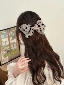 Rear view of a large cream mesh polka dot bow hair clip styled on a low ponytail